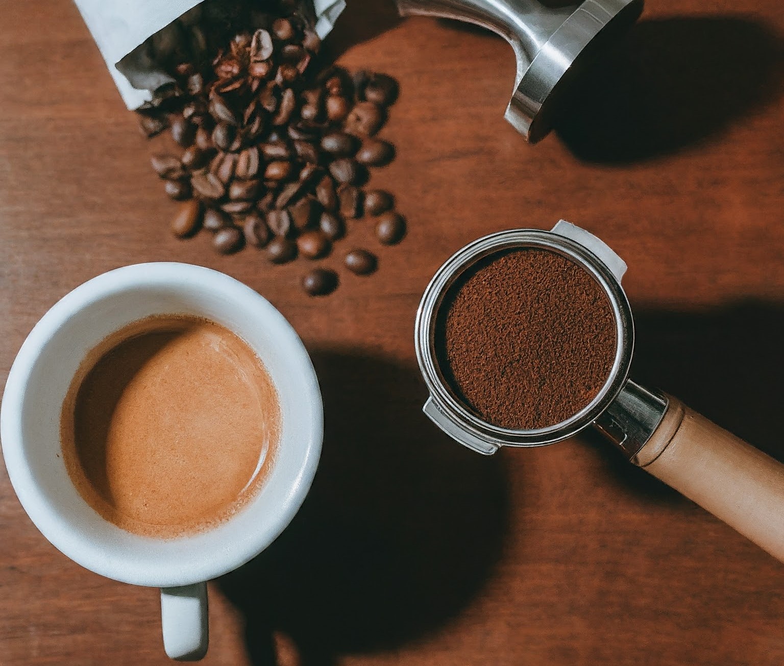 Freshly ground espresso beans beside a bag of whole beans and a burr grinder