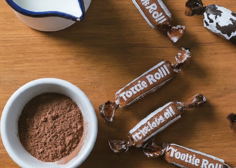 Close-up of Tootsie Rolls on a table with spilled milk, highlighting the blog post's exploration of Tootsie Roll ingredients including milk.