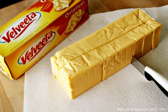 "Velveeta processed cheese block on a cutting board with slices next to it."